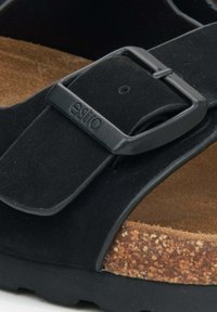 Zwarte sandal met een kurken voetbed, voorzien van een brede strap, verstelbare gesp en een suède-achtige bovenmateriaal. Plastic hardware detail.