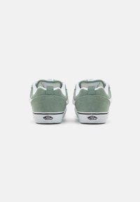 Grønne semskede sneakers med hvide detaljer, der har en polstret krave, flade snørebånd og en tekstureret gummisål prydet med logo.