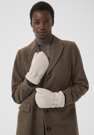 Teplé, krémovo sfarbené fleece rukavice s textúrovaným povrchom a bočnými zipsami, nosené s hnedým vlneným kabátom a šedým rolákom.