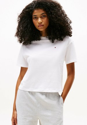 T-shirt bianca in cotone con maniche corte, scollatura rotonda e un piccolo dettaglio con logo. Abbinata a pantaloni felpati grigi chiari.