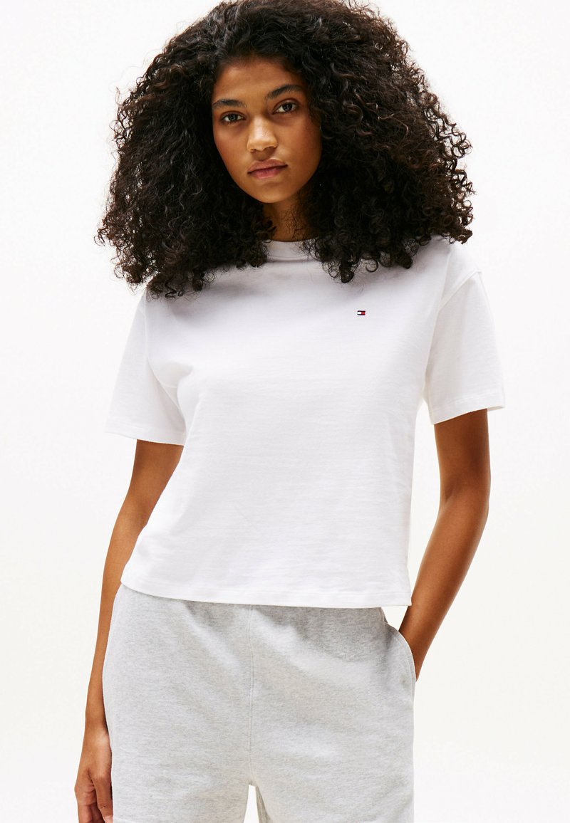 Witte katoenen T-shirt met korte mouwen, ronde halslijn en een klein logo detail. Gecombineerd met lichtgrijze joggingsbroek.