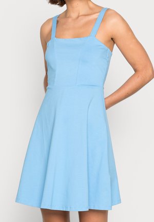 Femme portant une robe sans manches bleu clair, longueur genou, avec un décolleté carré et une taille cintrée, sur un fond uni.