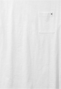T-shirt blanc à manches courtes, en tissu doux. Dispose d'une petite poche poitrine avec une couture horizontale et une surpiqûre noire contrastante en forme de "X".