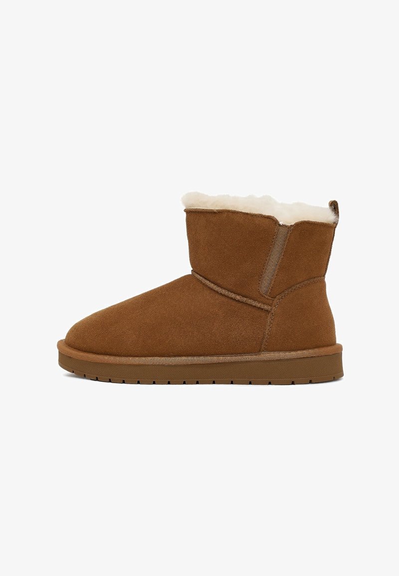 Brown suede ankle boot with a soft white fleece lining and a flat rubber sole, featuring a subtle stitching detail and minimal branding.