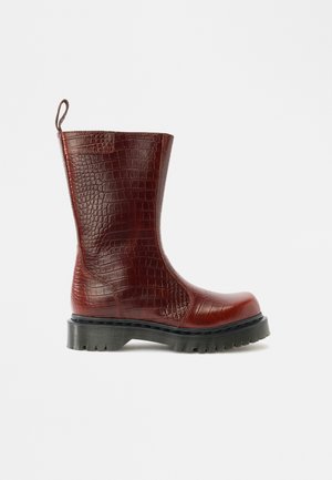 Bota de couro vermelho com estampado de crocodilo, bico redondo, acabamento texturizado e sola grossa de borracha. Apresenta uma tira para puxar na parte de trás.