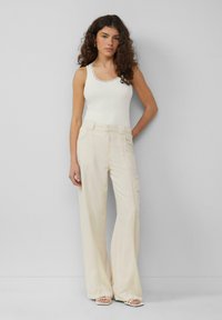 Lichtbeige wijde broek van zacht materiaal, met verschillende zakken en een relaxte pasvorm, gecombineerd met een aansluitend wit tanktop.