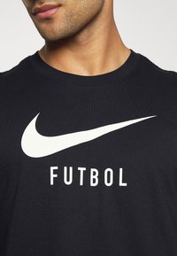 Homme portant un t-shirt noir avec un grand logo Nike blanc et le mot "FUTBOL" imprimé sous le logo.