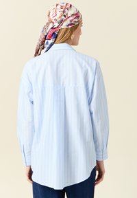 Camicia a strisce blu chiaro in cotone, con una vestibilità comoda, maniche lunghe, orlo curvo e una plissettatura sulla schiena per una maggiore libertà di movimento.