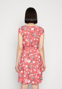 Robe fleurie corail, avec des manches courtes, un corsage ajusté et une jupe fluide. Le motif comprend des fleurs roses et bleues avec des feuilles vertes.