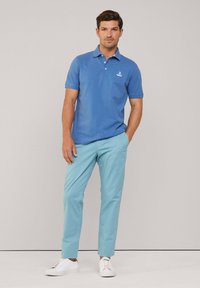 Niebieska koszulka polo z kołnierzykiem i małym logo, w zestawieniu z jasnoniebieskimi spodniami i białymi trampkami. Gładka tekstura i dopasowany krój.
