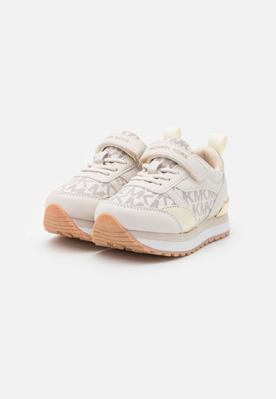 Witte sportschoenen met een gestructureerde bovenkant, voorzien van een zilveren logo, een klittenbandsluiting en een rubberen zool van gum met een lichte hak.