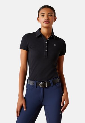 Polo noir avec col et patte de boutonnage à trois boutons. Présente un petit logo sur la poitrine gauche. Porté avec un pantalon d'équitation bleu marine et une ceinture noire.