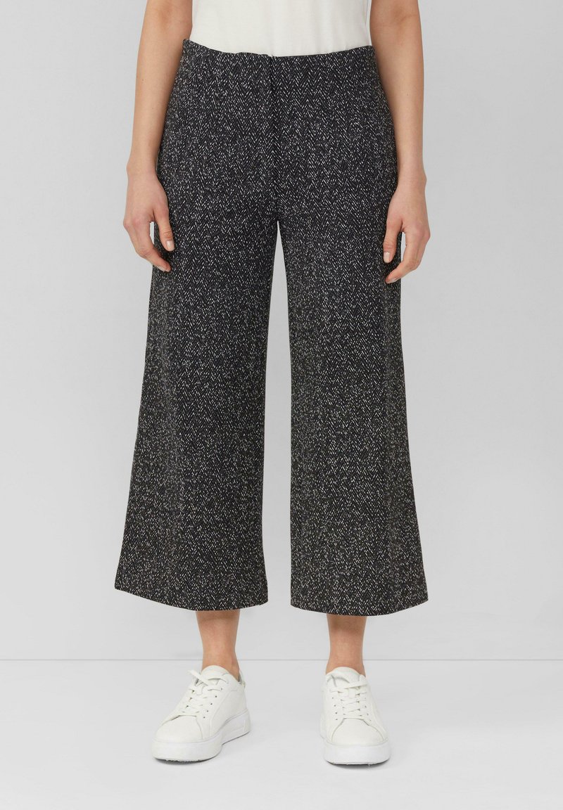 Pantalons large-jupe en pied de poule noir et blanc à taille haute, en tissu texturé, accompagnés de baskets blanches.