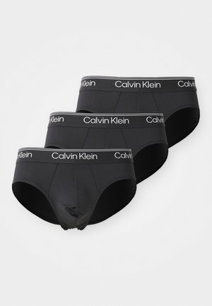 Sorte bomuldsunderbukser med elastisk talje, der har hvid "Calvin Klein" branding. Tre par stablet, der viser en glat tekstur og rundede ben.