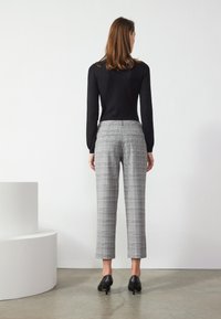 Haut noir à manches longues associé à un pantalon court en plaid gris. Le pantalon possède des poches arrière et une finition lisse et ajustée. Des escarpins noirs viennent compléter le look.