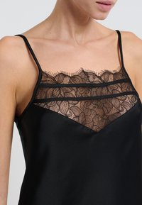 Camisole nera di raso con delicata rifinitura in pizzo sul collo, con tre strisce orizzontali in pizzo e spalline sottili regolabili.