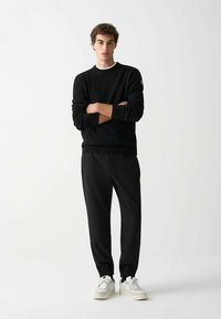 Zwart gebreide trui met ronde hals en geribbelde zoom, gecombineerd met zwarte joggingbroek en witte sneakers. Eenvoudig en gestroomlijnd ontwerp.