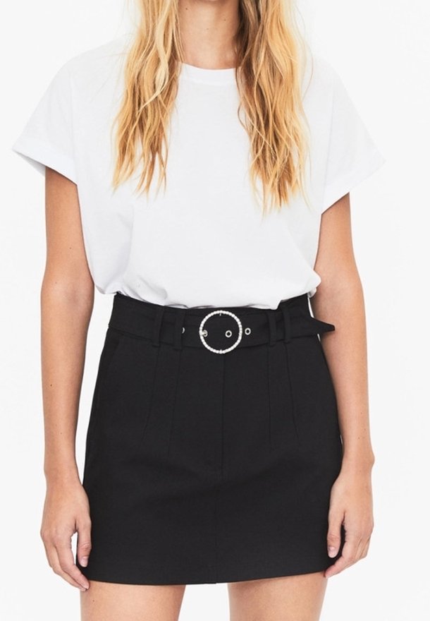 Kvinna i en vit t-shirt med kort ärm som är instoppad i en högmidjad svart kjol med ett runt spänne.