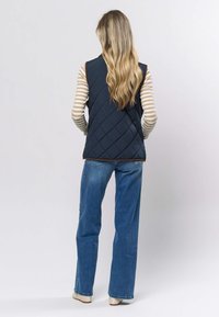 Marineblå quiltet vest med h øy hals, stylet over en stripete langermet genser. Kombinert med lyseblå jeans og kremfargede sko.