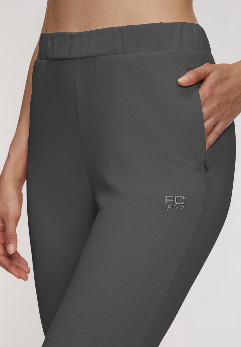 Gray athletic pants with a smooth texture, elastic waistband, side pockets, and an embroidered "FC 1972" logo near the hem.