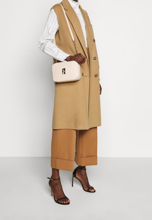 Gilet di lana beige con bottoni, camicia bianca a righe, pantaloni a gamba larga color cuoio, décolleté nere con cinturini e una piccola borsa rosa con dettaglio dorato.