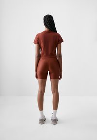 Short-sleeve rust top paired with rust shorts. Soft, stretchy fabric with a fitted design. Model wearing white socks and light gray sneakers.