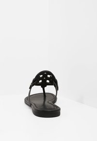 Sandales plates noires avec un design supérieur tissé, bout ouvert, fines lanières et semelle lisse. Style minimaliste sans embellissements.