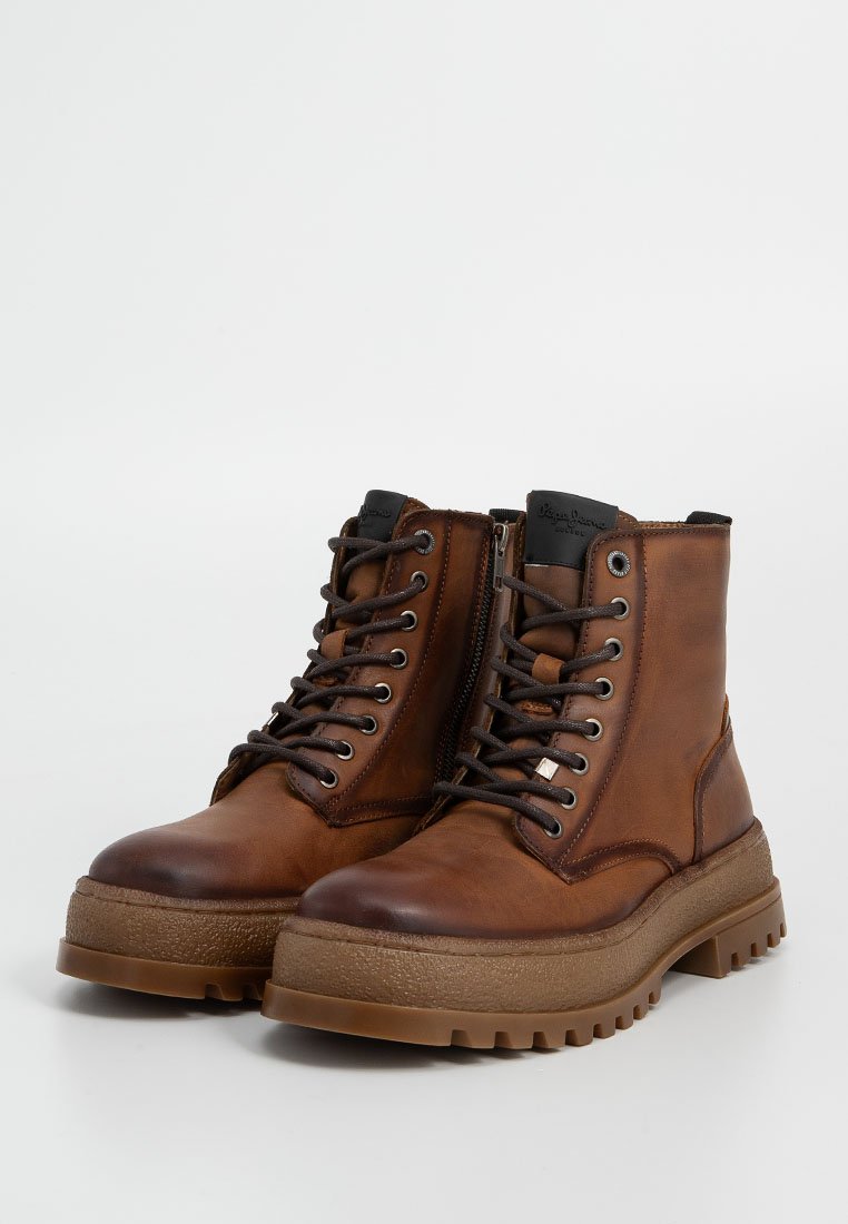 Botas de cuero marrón hasta el tobillo con punta redonda, cordones en la parte delantera, cierre de cremallera y suela de goma texturizada. Presentan costuras reforzadas y acentos de logo.