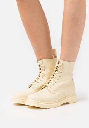 Cremefarvede læderankelstøvler med snørebånd, rund snude, tekstureret overdel og forstærket sål. Indeholder fremtrædende snørebånd og en trækflig bagpå.