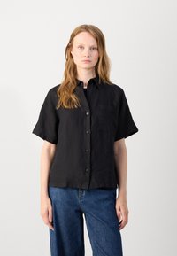 Svart linneskjorta med korta ärmar, en bröstficka och avslappnad passform, matchad med blå vida jeans.