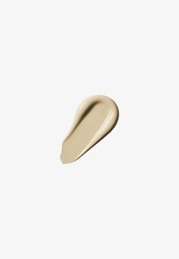 Glatter, beige flüssiger Creme-Tupfer mit glänzender Textur auf weißem Hintergrund.