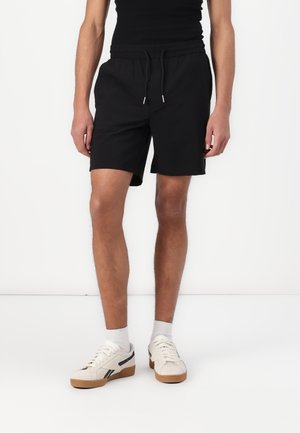 Black athletic shorts with an elastic waistband and drawstring, paired with white sneakers featuring black accents and gum soles.