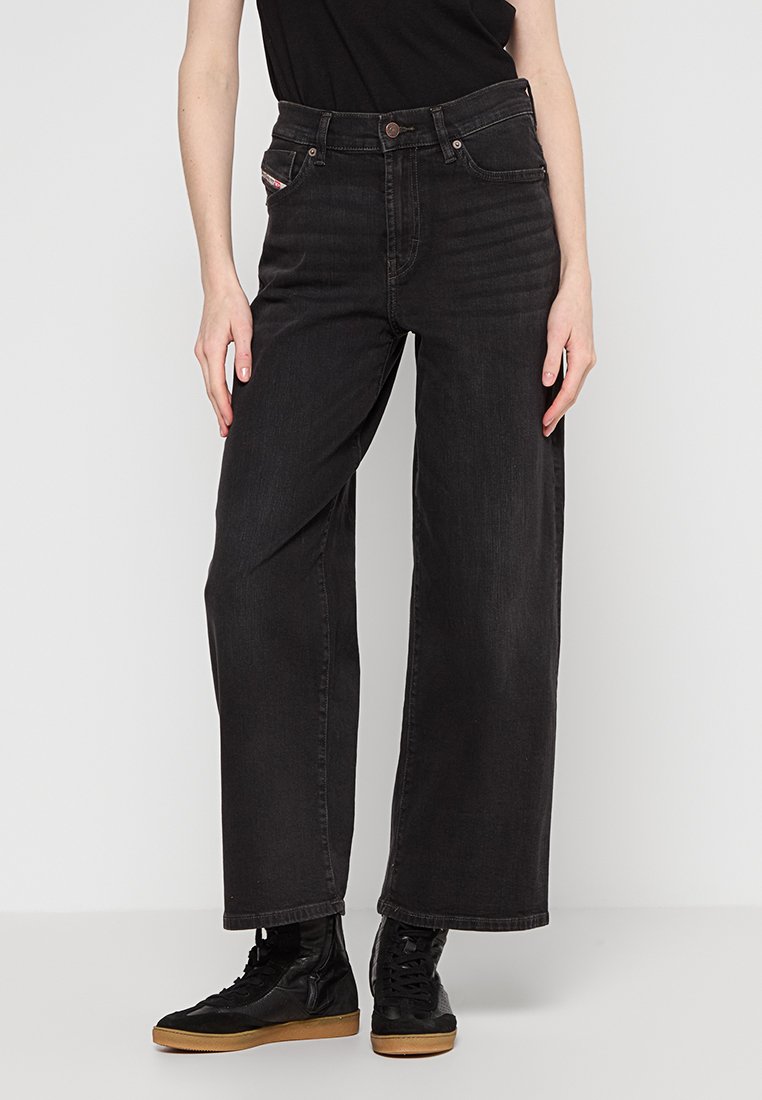 Jeans a gamba larga in denim nero con vita alta, caratterizzati da tasche frontali e dettagli di cucitura sottili. Abbinati a sneaker nere alte.