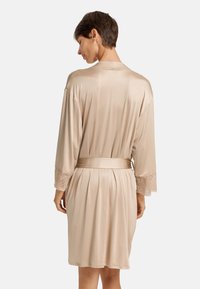 Robe in satin beige con maniche a tre quarti, caratterizzata da dettagli in pizzo sui polsini, vita con cintura e dettagli plissettati sulla schiena.