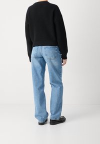 Pull en tricot côtelé noir, coupe décontractée. Jean bleu clair à jambes droites. Chaussures noires. Détails minimaux avec des accents de couture sur les manches.