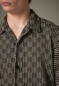 Camicia con bottoni frontali caratterizzata da un motivo a zigzag bianco e nero, design con colletto e tessuto texturizzato. Bottone nero sul petto.