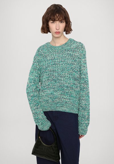Green knitted sweater with a loose fit, ribbed crew neckline, and textured pattern. Paired with a small black handbag.