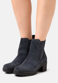 Bottines en daim noir avec panneaux latéraux élastiques, bout rond et semelle noire épaisse. Des détails cousus rehaussent le design.