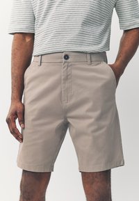 Beige shorts met een plat voorpand, riemlussen en een enkele knoopsluiting. Het materiaal lijkt glad, met zijzakken en een gestructureerde pasvorm.