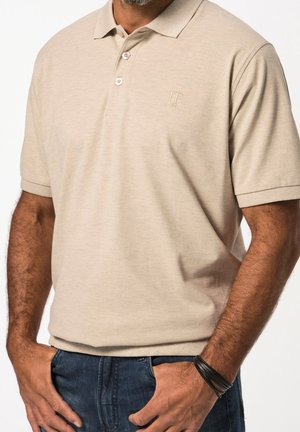 Homme portant un polo beige à manches courtes avec des boutons, un jean foncé et un bracelet en cuir noir au poignet.