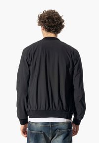 Giubbotto bomber nero con polsini e orlo elasticizzati, realizzato in tessuto liscio e leggero. Presenta un design semplice e minimalista senza loghi visibili.