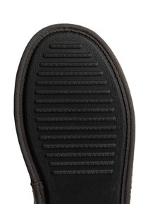 Semelle de chaussure en caoutchouc noir avec des rainures horizontales et des accents texturés, ornée d'une bordure en tissu sombre autour du bord pour une durabilité accrue.