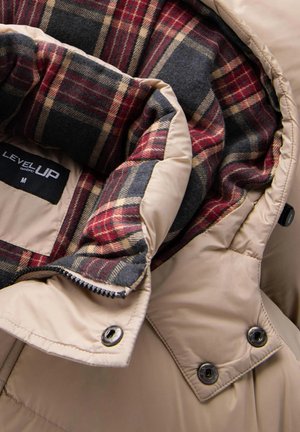 Béžová péřová bunda s prošívaným exteriérem a podšívkou v červeno-modro-hnědém kostkovaném vzoru. Obsahuje zipové zapínání a akcenty s druky.