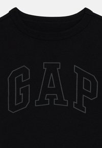 Juodas medvilninis marškinėliai su apvaliu kaklu ir tonaus pilko spalvos "GAP" logotipo dizainu, atspausdintu priekyje. Minkšta tekstūra ir klasikinis siluetas.