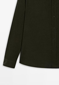 Camicia a maniche lunghe verde scuro con apertura a bottoni, caratterizzata da una texture liscia e orlo curvo. I bottoni sono neri e distribuiti uniformemente.
