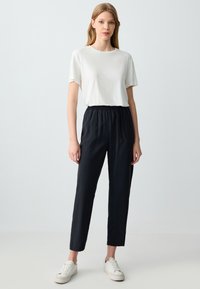 T-shirt blanc à manches courtes associé à un pantalon noir à taille élastique et des baskets blanches. Texture de tissu lisse et coupe décontractée.