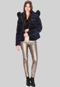 Tengerészkék steppelt pufi dzseki szőrmével bélelt kapucnival és cipzáras záródással. Aranyfényű, testhez simuló nadrággal és fekete bokacsizmával párosítva.