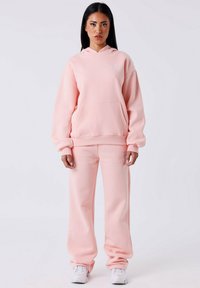 Roze katoenen hoodie met een voorzak en bijpassende sweatpants. Heeft een relaxed fit en een geborduurd logo aan de bovenkant aan de linkerkant.