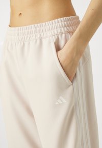 Helle rosa Sporthosen mit einem elastischen Bund, seitlichen Taschen und drei weißen Streifen entlang der Seite. Hat ein kleines weißes Logo.