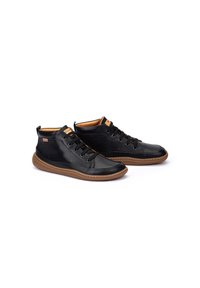 Zapatos altos de cuero negro con suelas de goma texturizada marrón, con diseño de cordones y acentos en contraste en beige en el cuello y la lengüeta.